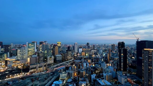 UMEDA, OSAKA, JAPAN : Aerial high angle sunset view of CITYSCAPE of OSAKA. View of buildings and street around Osaka and Umeda station. Wide view time lapse zoom out shot, dusk to night.