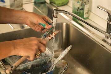 Detail of mature woman's hands cleaning brushes under tap water after painting.
