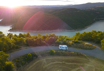 Awesome aerial drone view of an incredible lake road with a van driving it at sunset.