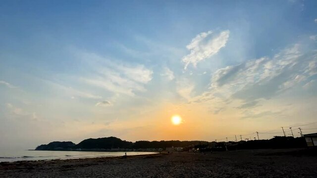 KAMAKURA, KANAGAWA, JAPAN - JUNE 2021 : YUIGAHAMA beach (Ocean or sea). View of magic hour sky and sun going down. Wide view time lapse shot at sunset time.