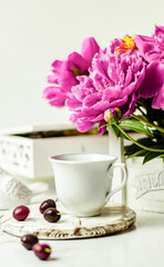 Obraz na płótnie Canvas Shabby chic tea. A cup of tea on a white wooden tray with a cherry nearby. Peonies are in a white box. Blurred background