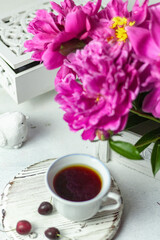 Shabby chic tea. A cup of tea on a white wooden tray with a cherry nearby. Peonies are in a white box. Blurred background
