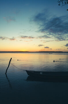 Small boat anchored on the shore of the lake during a day's sunset with some clouds. Calm waters