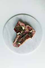Raw rib eye, t-bone steak of beef on a board with a meat cleaver, onion and seasonings