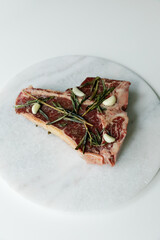 Raw rib eye, t-bone steak of beef on a board with a meat cleaver, onion and seasonings