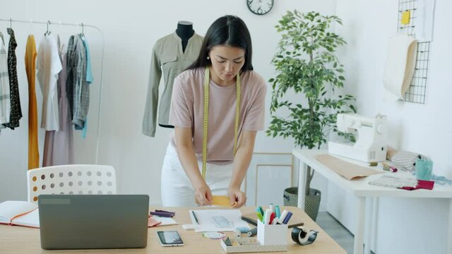 Slow motion of young Asian woman clothes designer choosing material and color for new garment working in studio alone. People and occupation concept.