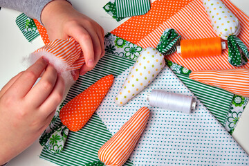 A child is making  a fabric carrot from multicolor fabrics. Craft for children. Easter decoration, gift.