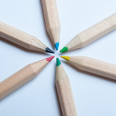Colorful wooden pencils arranged in a symmetrical radial star shape, seen from above. White background. Concept school.