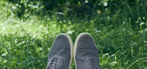 Young man in gray sneakers on green grass in field. Gray sneakers on green grass.
