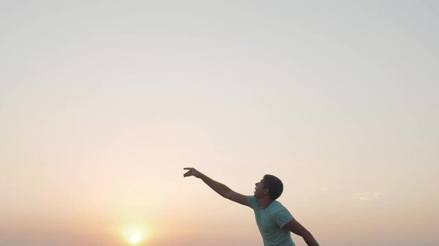 man in cheerful mood throwing paper airplane in field on sunset on background of clear sky, concept of active rest outdoors and relaxation, toy of childhood