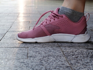 A foot in a pink sneaker stands on a paving slab in the evening lighting