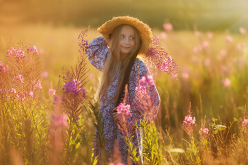 A child in a hat with a bouquet flowers. A girl in dress, a straw hat, with a bouquet is standing on a flower meadow. Summer time.