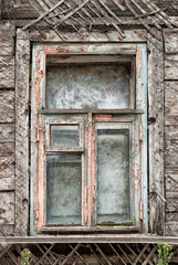 Fototapeta na wymiar Wooden window without platbands with stripped paint in an old residential building in Russia