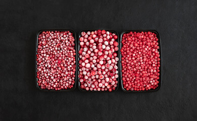 Set of frozen berries on a black background. Cranberries, red currants and cowberries in plastic containers. View from above.