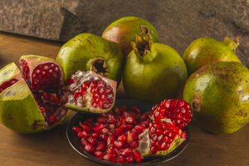 Pomegranate in segments and whole, showing its presentation in a different way, on a wooden table and a stone background.