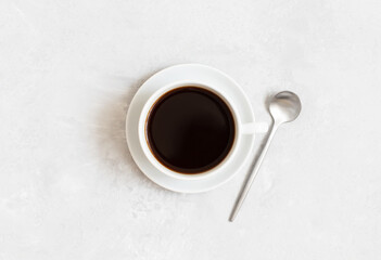 Black coffee in a cup and silver spoon on a white concrete background. Top view, flat lay.