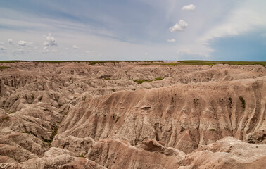 Badlands National Park, SD, USA - June 1, 2008: Wide landscape of beige-brown mountains of geological deposits cut by canyons under blue cloudscape.