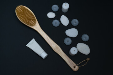 Spa still life with scented candles, treatment stones, cream and massage brush against a dark background. Flyer.