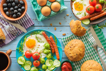 composition of rustic breakfast, eggs and sausage with vegetables, wooden background, top view
