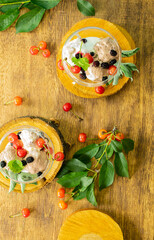 Rustic breakfast: ice cream in bowls, mint, cherries, mulberries on a wooden background, a bouquet of roses, top view
