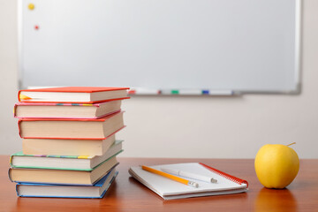 Concept of school education. School desk with a pile of books, exercise book and an apple with an empty board on the background