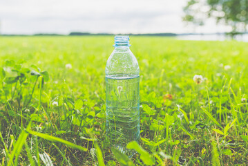 Plastic Bottle fresh transparent water on green grass on sunny day.Nature texture, green blurred background, wallpaper.