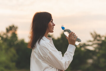 Girl drinks water from a plastic bottle.young caucasian woman in nature forest in woods while holding bottle of water