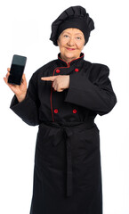 woman chef in black uniform. apron, shirt, hat. elderly woman. The food preparation specialist holds the phone and points at it. make an order in a restaurant online. white background, isolated