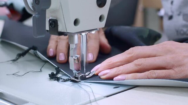 Woman Tailor Seamstress Working In Clothes Factory - Sews Black Fabric On Sewing Workshop. Female Dressmaker Hands With Manucure Makes Clothes. Sewing Machine Closeup. Real People Hand Made Craft Job.