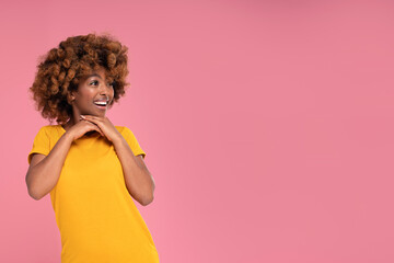 Happy beautiful afro girl smiling and looking aside on a copy space on pink pastel studio background. Colorful photo. Real people emotions. Sale.