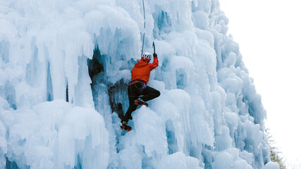 Naklejka premium Man climbing on a frozen steep slope, passing between large bumps, ridges, and icicles