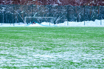 field for playing football in winter, artificial grass on cleared of snow in the distance gate