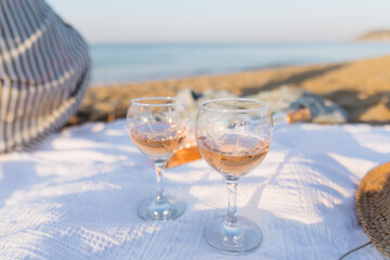 Summer picnic on the beach at sunset. Young woman with glass of rose wine. Weekend picnic. Close up.