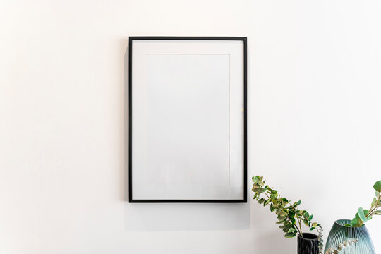 Home decoration, empty black frame, poster, white canvas, mock up on a white wall, living room, template front view