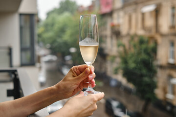 Girl with a wine glass on the balcony. Drinks white wine and enjoy the moment. A celebration holiday alone. Relaxed lifestyle. Happy woman rest after work. Beautiful European courtyard