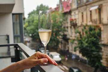 Girl with a wine glass on the balcony. Drinks white wine and enjoy the moment. A celebration holiday alone. Relaxed lifestyle. Happy woman rest after work. Beautiful European courtyard