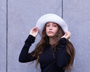 Medium shot of beautiful teenager with long chestnut hair dressed in long-sleeved black dress holding a white straw hat on her head © Anne Richard