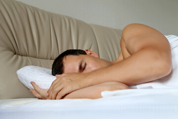Muscular man sleeping on a bed with his hand under the pillow