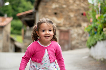 Niña con vestido de flore y chaqueta rosa jugando jovial con un peluche de perrito.