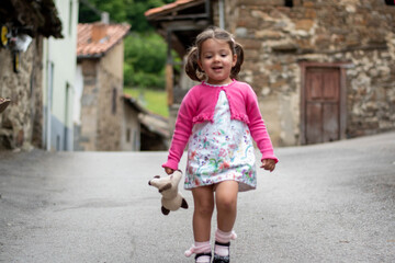 Fototapeta premium Niña con vestido de flore y chaqueta rosa jugando jovial con un peluche de perrito.