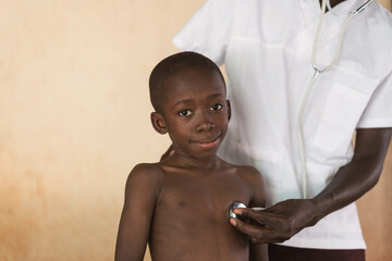 Smiling African black boy getting examined with a stethoscope by African doctor.