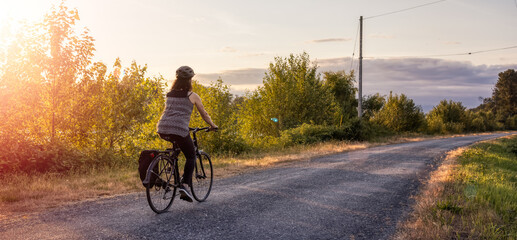 Adventurous White Cacasusian Woman riding a bicycle on a road. Sunny Summer Sunset. Barnston...