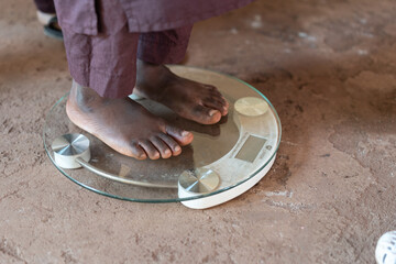 African black boy standing on scale to measure his own weight.