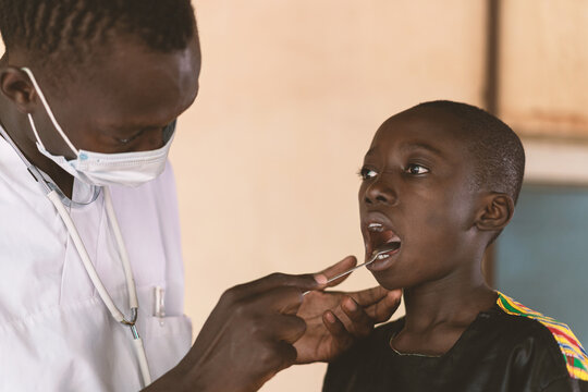 African cute boy opens his mouth to get an African doctor examining his mouth and throat.