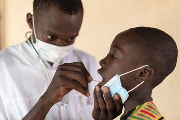 Testing for disease: African black male nurse checking mouth of young African child in Bamako, Mali.