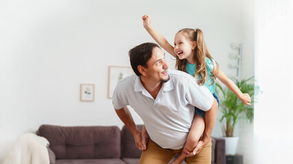 Happy positive cheerful dad is playing with his little charming daughter at home. The man circles and throws the girl up. A dynamic image. Copy space