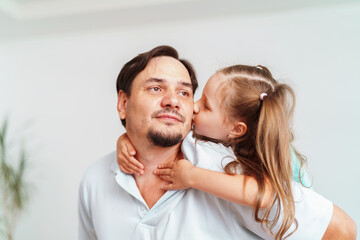 Fototapeta premium Happy positive cheerful dad is playing with his little charming daughter at home. The man circles and throws the girl up. A dynamic image. Copy space
