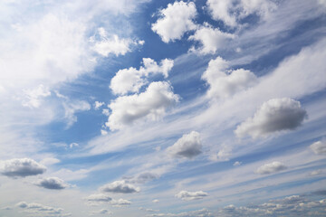 Blue sky covered with white cumulus and cirrus clouds. Summer cloudscape, beautiful weather background