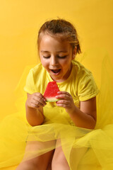 Happy caucasian girl holding a piece of watermelon she is going to eat with her hands. Yellow background with vertical copy space. Fresh and healthy fruit concept.