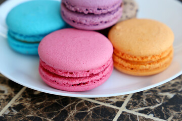 Macaroons in a white plate close up, colorful sweets. Strawberry, blueberry, vanilla and orange almond cookies with filling on a table